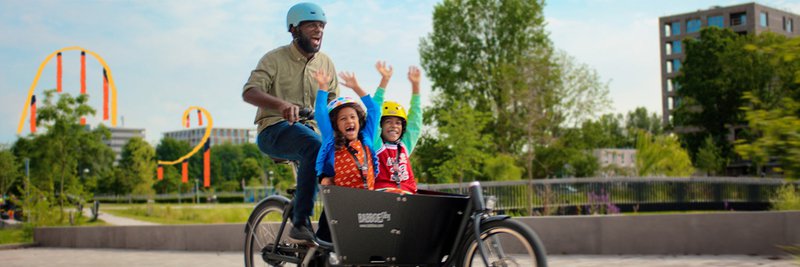 Das Foto zeigt einen Vater der in einem Babboe E-Lastenrad zwei Kinder transportiert.